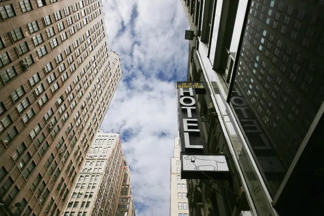Looking up at tall city buildings and a vertical HOTEL sign on a street under a cloudy sky.