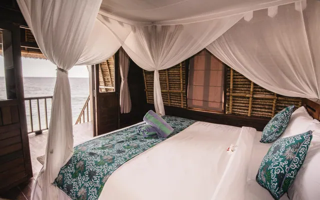 A bedroom with a canopy bed under white mosquito netting, with an open doorway onto a balcony overlooking the sea.