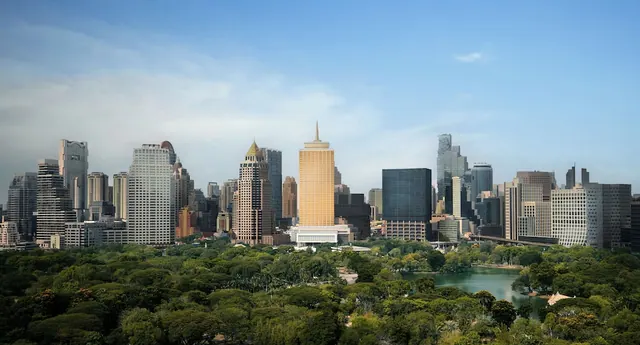 A wide view over a green park and small lake toward a skyline of high-rise towers under a partly cloudy blue sky.