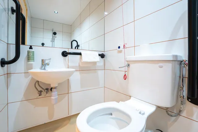 A white bathroom with a wall-mounted basin, a toilet with a cistern, black grab rails and a towel on a rail.