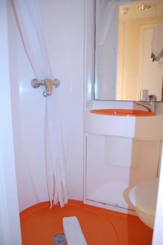 A small bathroom with an orange shower tray, a white shower curtain, an orange wash basin and a white toilet beside it.