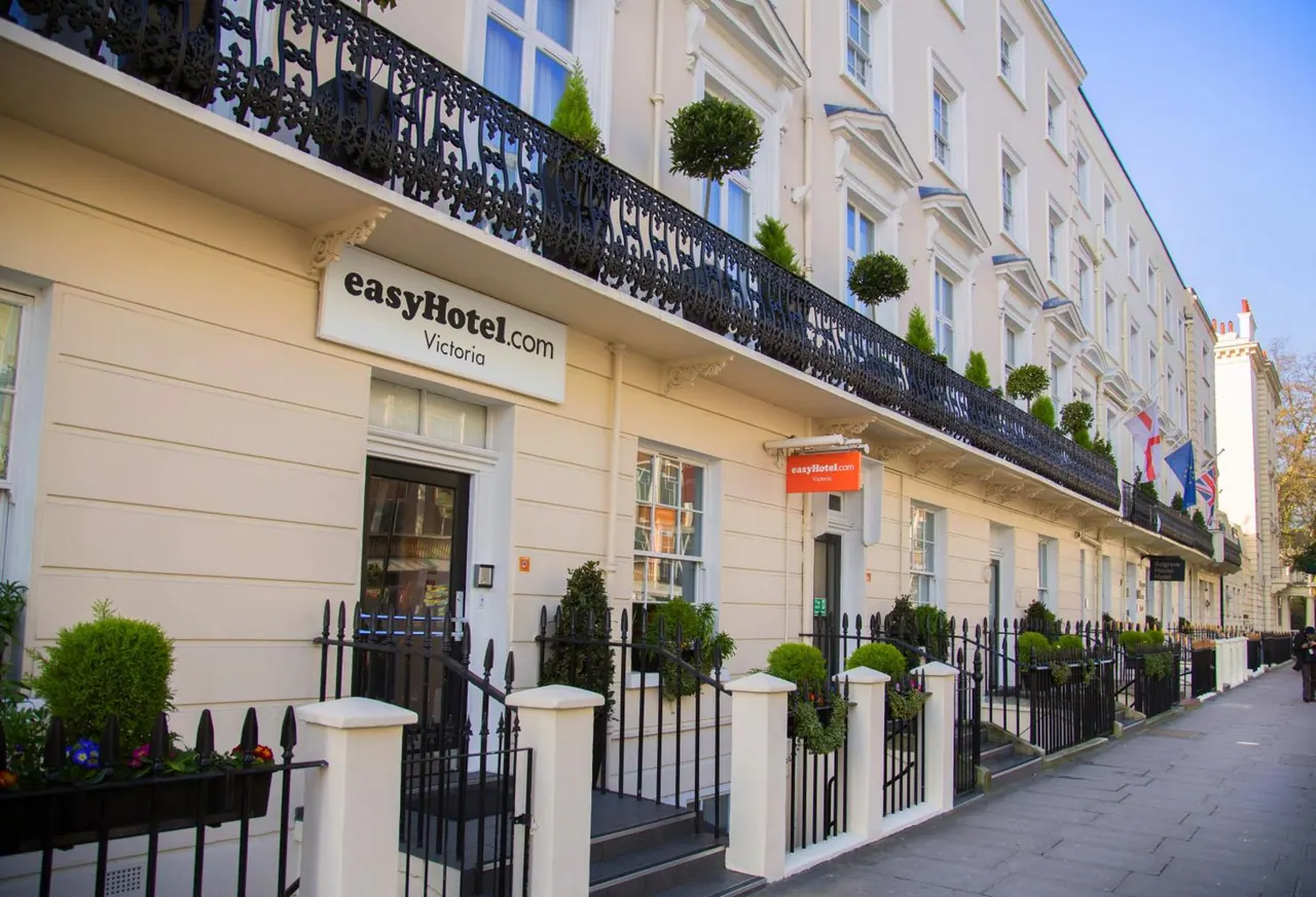 The cream-coloured front of a terraced hotel building with an easyHotel.com sign, black iron balcony railings, flower planters and a pavement along the street.