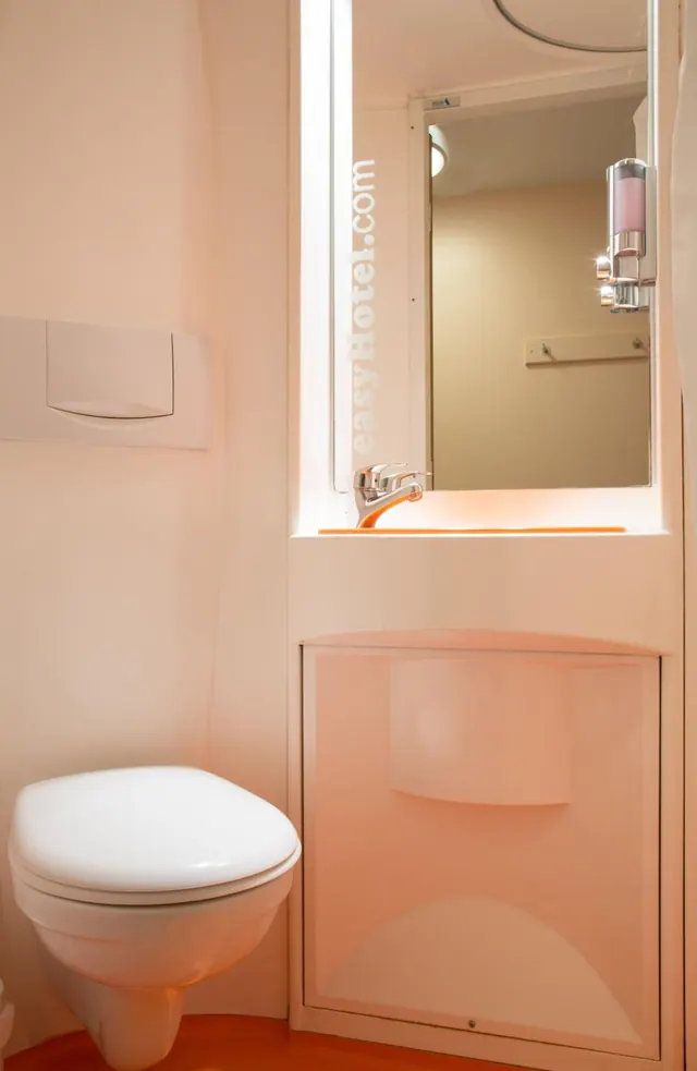 A small bathroom with a wall-mounted toilet, a basin with a chrome tap, a mirror and a wall-mounted soap dispenser.
