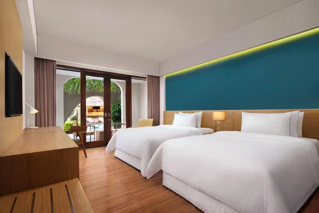A bedroom with two twin beds, a teal feature wall with backlighting, a wall-mounted television, and glass doors opening onto a garden and pool outside.