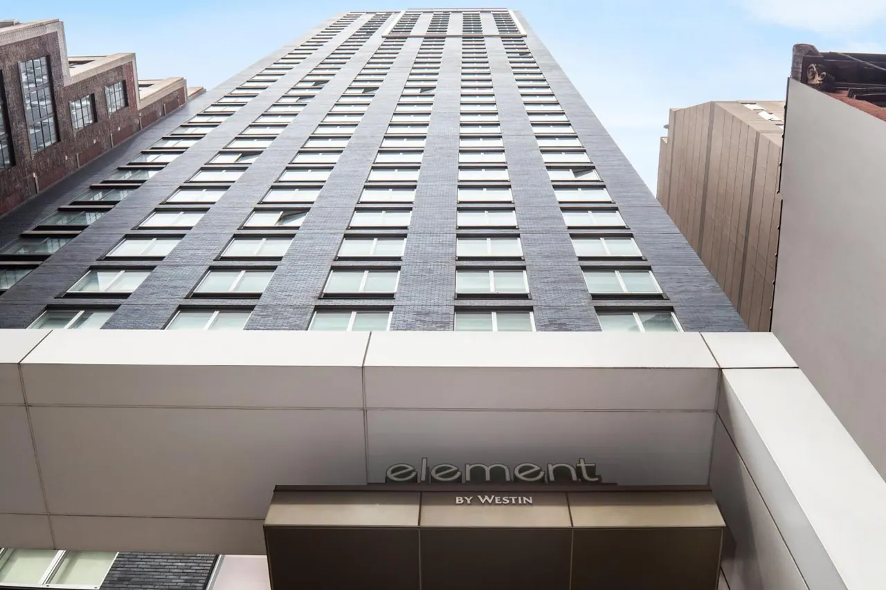 Upward view of a tall hotel tower with grey window panels, with an Element by Westin sign above the entrance.