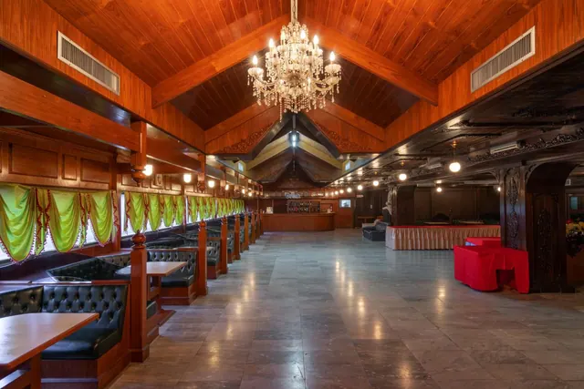 A large dining hall with a wooden ceiling, a crystal chandelier, tufted leather booth seating along the left wall and a bar at the far end.