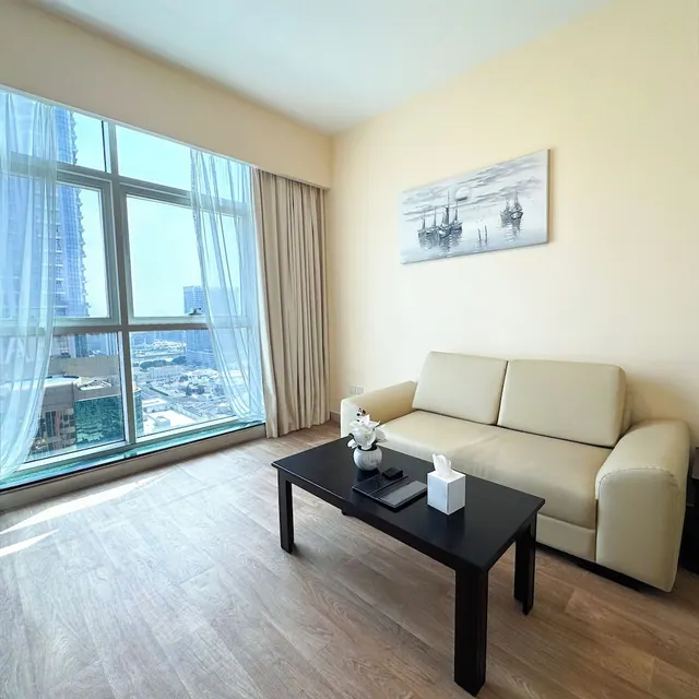 A living room with a cream leather sofa, a black coffee table and large windows looking out over city buildings.