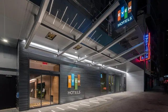 Night view of the EVEN Hotels building entrance with illuminated signage, a overhead canopy and a glass front door.