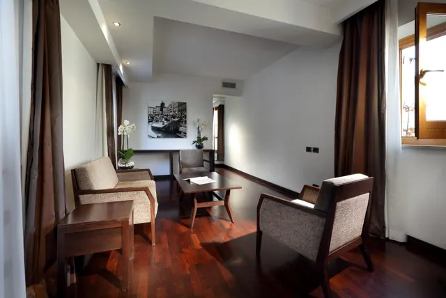 A living area with two upholstered armchairs, a sofa, a wooden coffee table, and a console table with orchids beneath a framed black and white photograph.