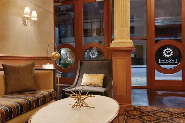 A lobby seating area with a striped sofa, a dark armchair, a round marble table and glass doors bearing a LeSoleil sun logo.