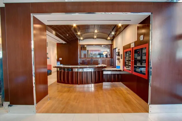 A wood-panelled hotel reception area with a curved front desk, a coffered wooden ceiling and red fire alarm panels on the right wall.