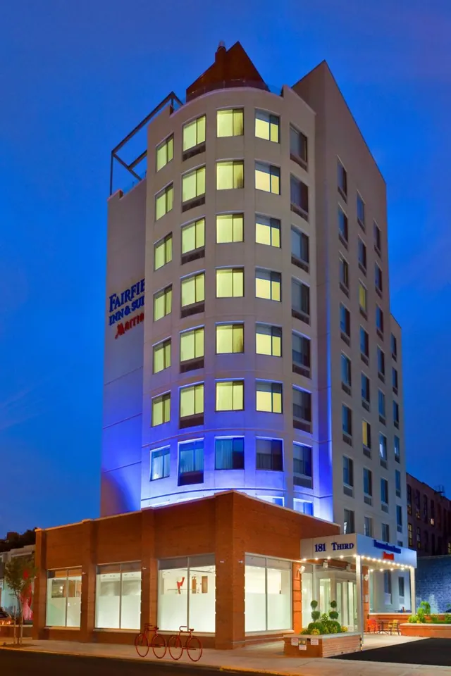 Exterior of a multi-storey hotel building at dusk with illuminated windows, a blue-lit facade and a brick ground floor with 181 Third signage.