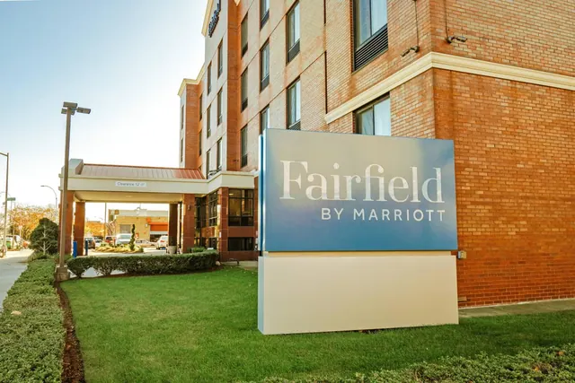 A brick hotel building with a Fairfield by Marriott sign on a lawn, and a covered driveway entrance to the left.