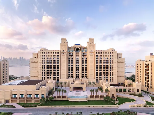 Elevated view of a large cream-coloured hotel building with arched details and a small pool and landscaped grounds in front, with water visible on both sides.