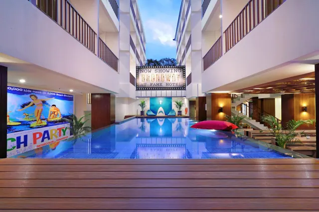 A rectangular swimming pool sits in an open courtyard framed by hotel balconies, with a wooden deck in the foreground and a Broadway-themed sign above the far end.