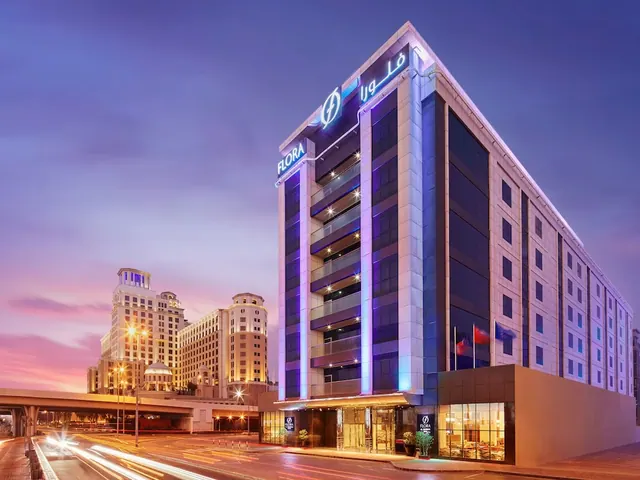 Exterior of the Flora hotel building at dusk, with illuminated signage and traffic light trails on the road below.