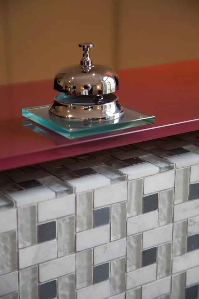 A chrome service bell sits on a glass tray on a red glass counter with a mosaic tiled front.
