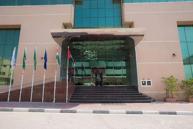 Straight-on view of the hotel's front entrance, with a set of dark steps leading up to glass doors and a row of national flags on poles to the left.