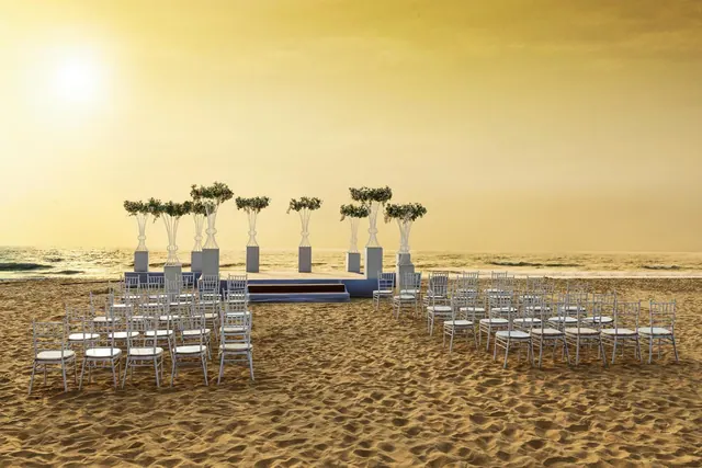 A decorated wedding seating area is arranged on a sandy beach beside the sea.