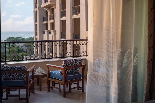 A private balcony with two wooden armchairs, a small side table holding a tea set, and the sea visible beyond the iron railing.