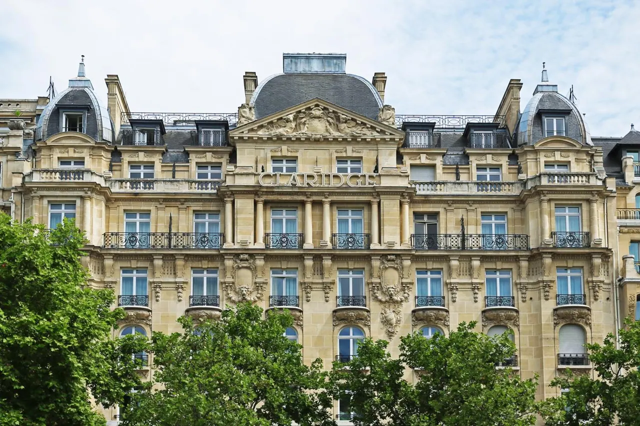 The ornate Claridge hotel façade is shown above a row of leafy trees.