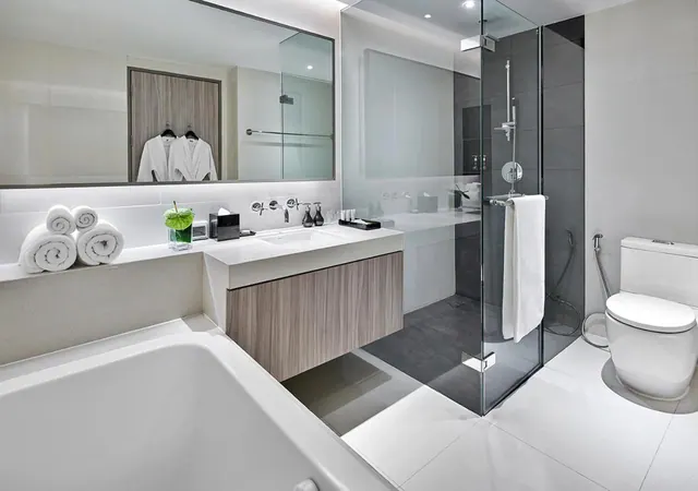 A bathroom with a built-in bathtub in the foreground, a floating vanity with a basin, a glass-walled walk-in shower, and a toilet beside a handheld bidet spray.