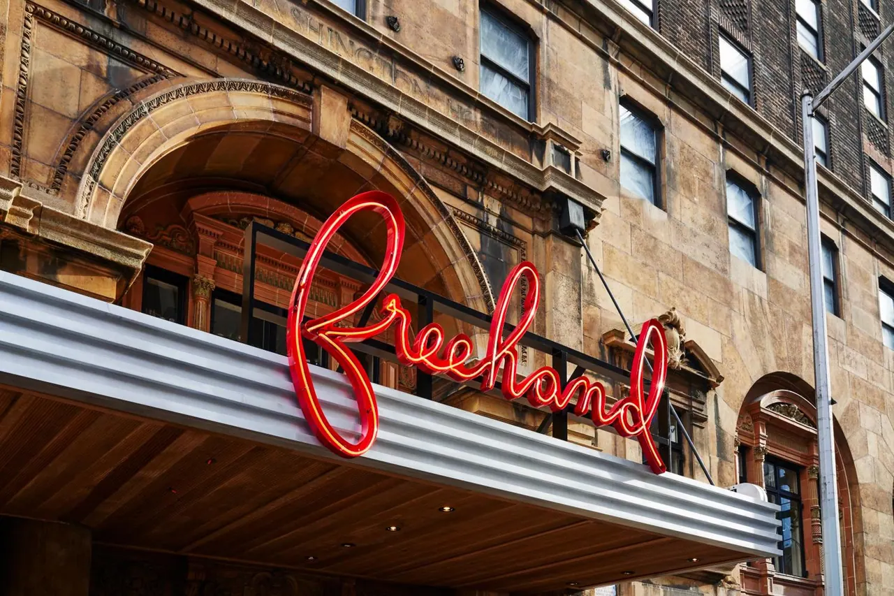 A red neon Freehand sign hangs above the entrance canopy of a stone building with arched windows.