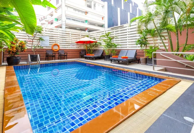 A small tiled swimming pool with sun loungers, an orange parasol and palm trees in a courtyard beside a multi-storey building.