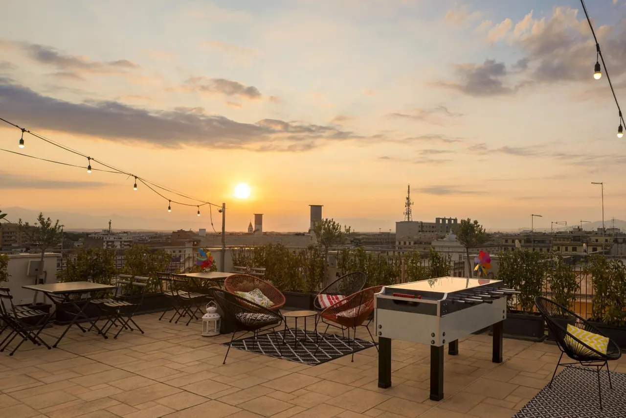 A rooftop terrace at sunset with outdoor chairs, a foosball table, string lights and a view over the city skyline.