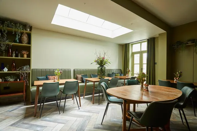 A dining room with green banquette seating, wooden tables and green chairs under a skylight.