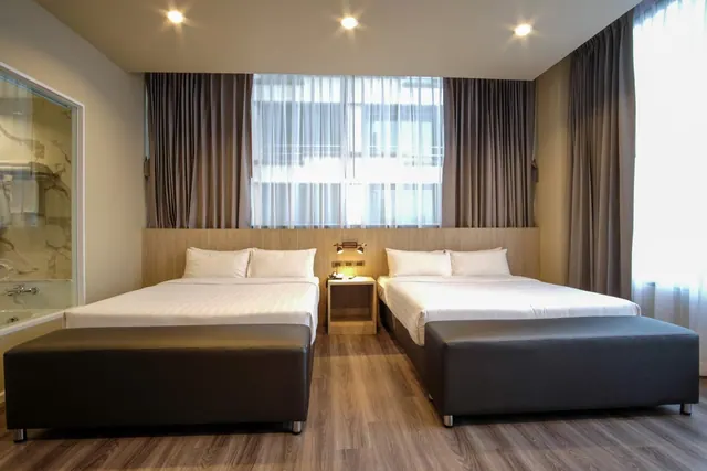 A bedroom with two double beds, each with a dark bench at its foot, a bedside table between them, and a glimpse of a marble bathtub at the left edge.
