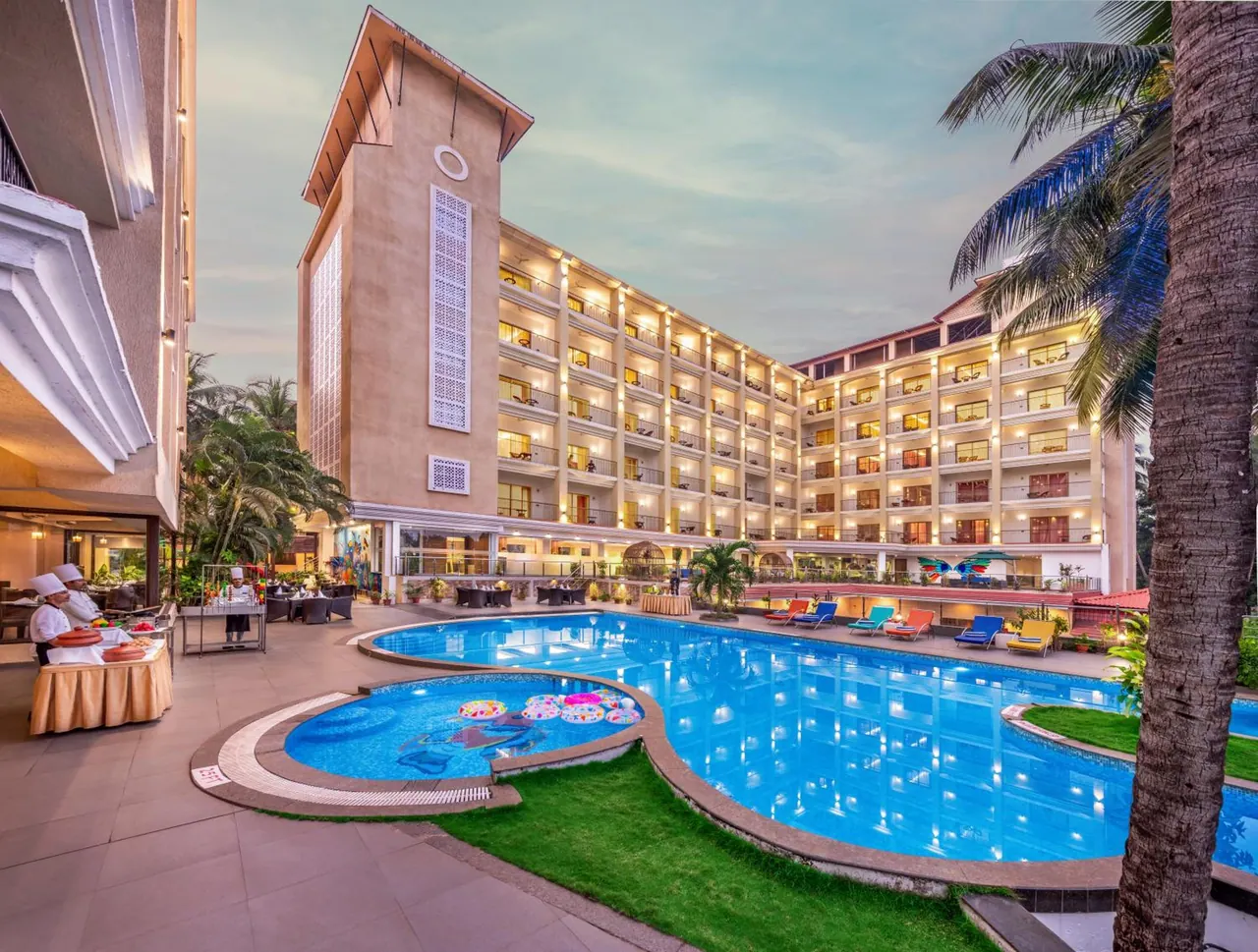 A large outdoor pool courtyard is surrounded by the hotel buildings, loungers, palm trees and a buffet setup.
