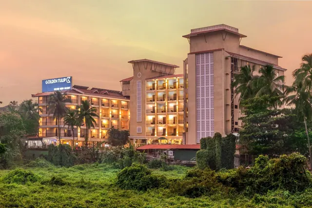 The Golden Tulip Goa hotel building is shown among lush tropical vegetation at sunset.