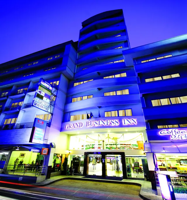 Night exterior of the Grand Business Inn building with an illuminated blue facade, entrance canopy and street signage.