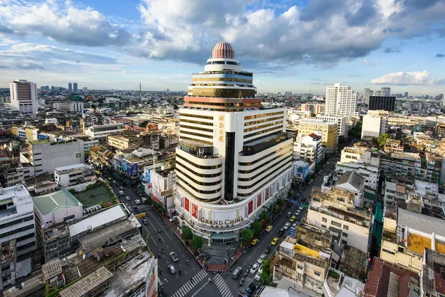 Aerial view of the Grand China Hotel tower rising above a dense city street with traffic under a partly cloudy sky.