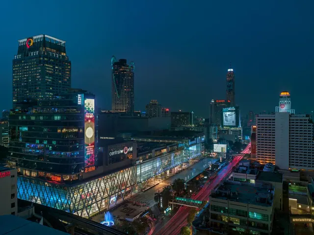 Night view over the Central World mall and surrounding Bangkok skyscrapers, with light trails on the road below.