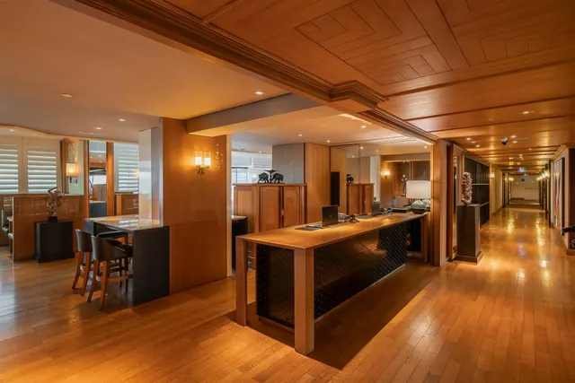 A lobby with a wooden reception counter, a high-level wood-panelled ceiling, a high bar table with stools on the left, and a long corridor running off to the right.