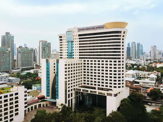 Aerial view of the Grand Mercure Atrium hotel tower with a gold curved rooftop, surrounded by high-rise buildings and trees under an overcast sky.