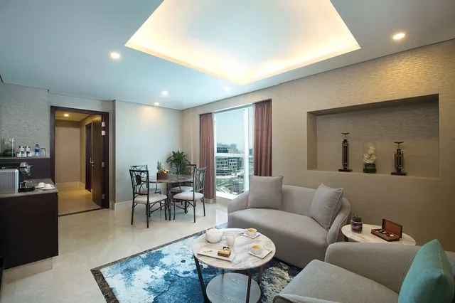 A living area with grey sofas, a round marble coffee table, a dining table by a tall window, and a coffee machine on a side counter.