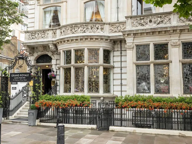 The ornate stone facade of the Grand Royale London Hyde Park hotel, with a black iron fence, flower planters and a street sign on the pavement.
