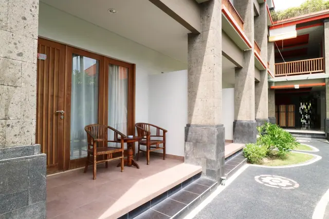 A private ground-floor terrace with two wooden chairs and a small round table beside wooden glass doors, next to stone pillars and a paved walkway.