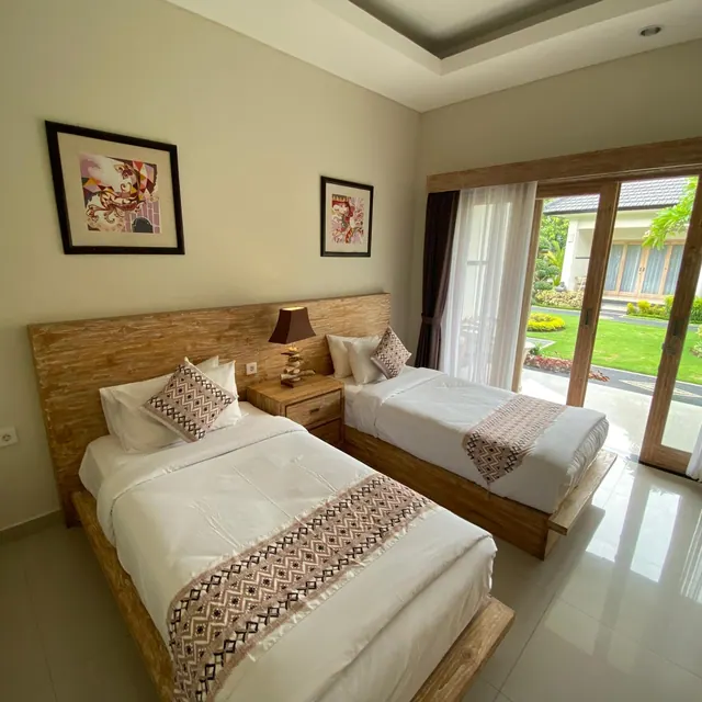 Two single beds with wooden headboards and patterned runners sit in a bedroom with sliding glass doors that open onto a lawn and garden.