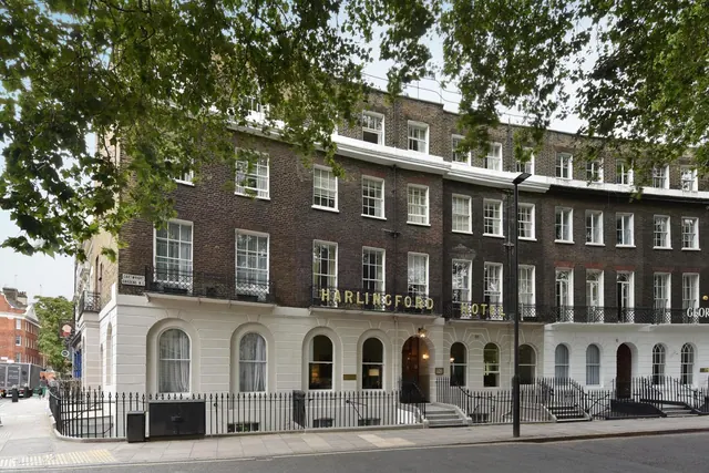 The hotel's brick and white-stucco Georgian terrace front is seen from the street, with black iron railings at ground level and tree branches across the top of the frame.