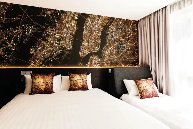 A bedroom with a double bed and a single bed, a wall mural of city lights at night, and cushions printed with a London map.