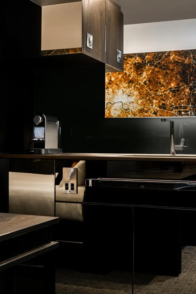 A dark kitchenette with a coffee machine, a chrome tap and a backsplash printed with a map of London.