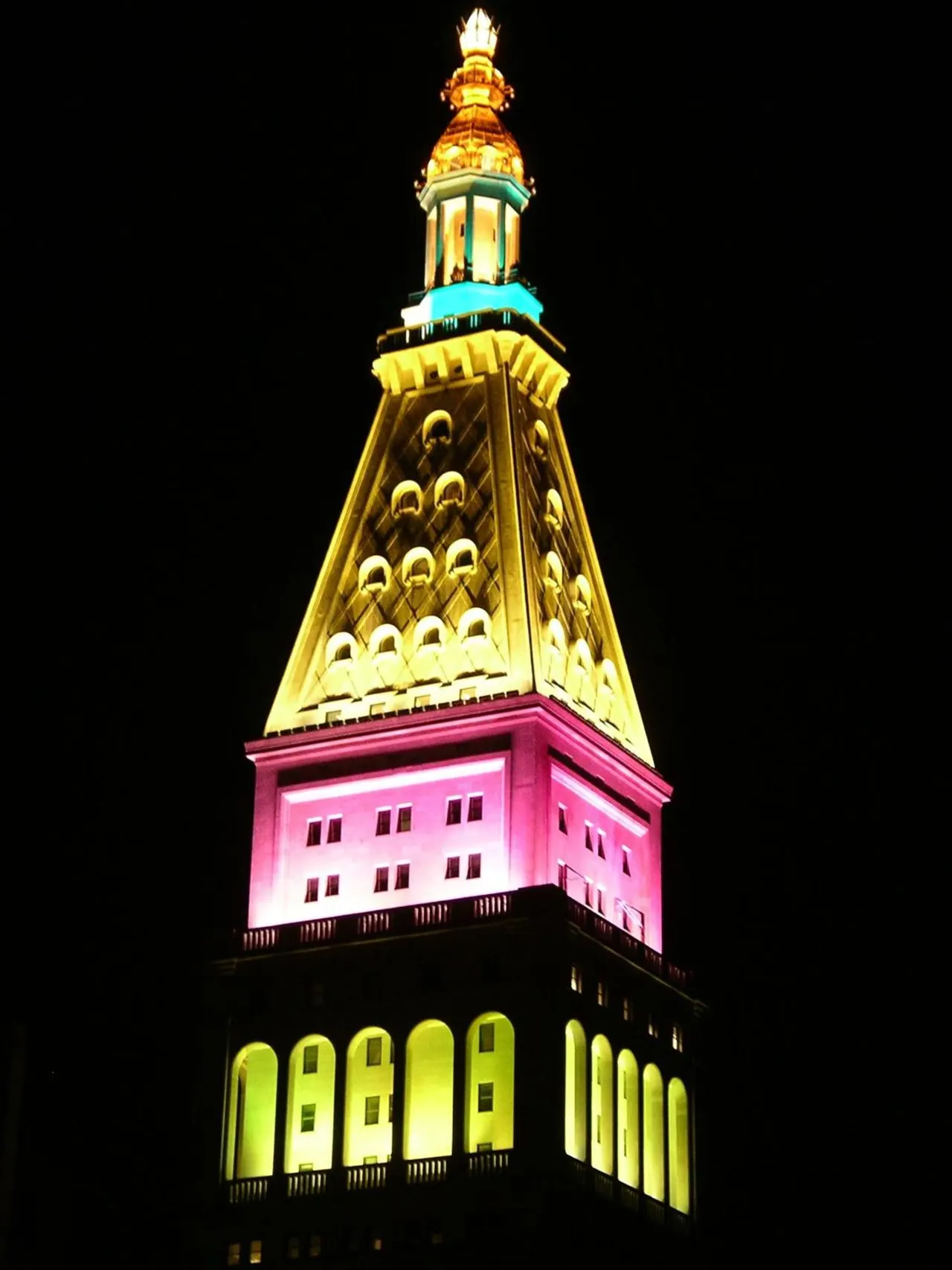 The illuminated Metropolitan Life Tower, with its pyramid roof and multicoloured lighting, stands against a black night sky.