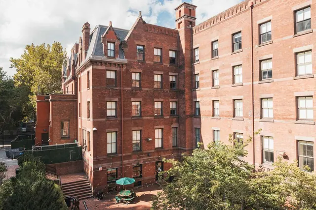 A multi-storey red brick building with arched gables and a courtyard containing a table with a green umbrella, photographed from above.