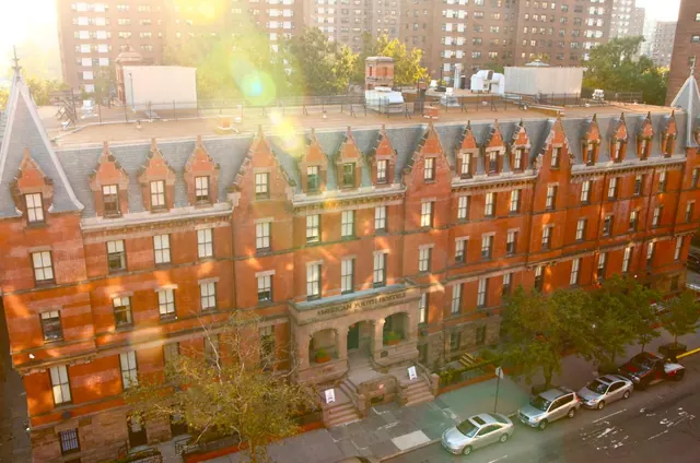 Elevated view of a red brick building with an American Youth Hostel sign over its entrance, with parked cars along the street below.