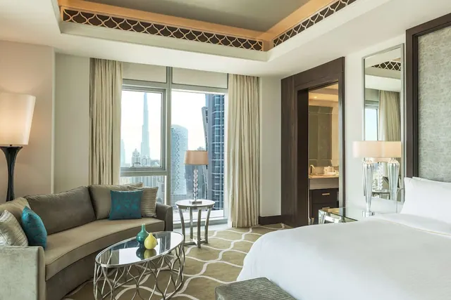 A bedroom with a king bed, a curved sofa and a window view of the Burj Khalifa and surrounding skyscrapers.