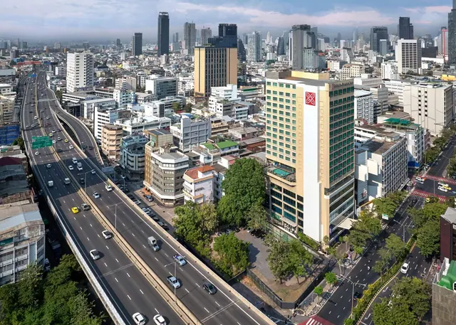 Aerial view of a high-rise hotel tower beside a multi-lane elevated road and dense city buildings in Bangkok.